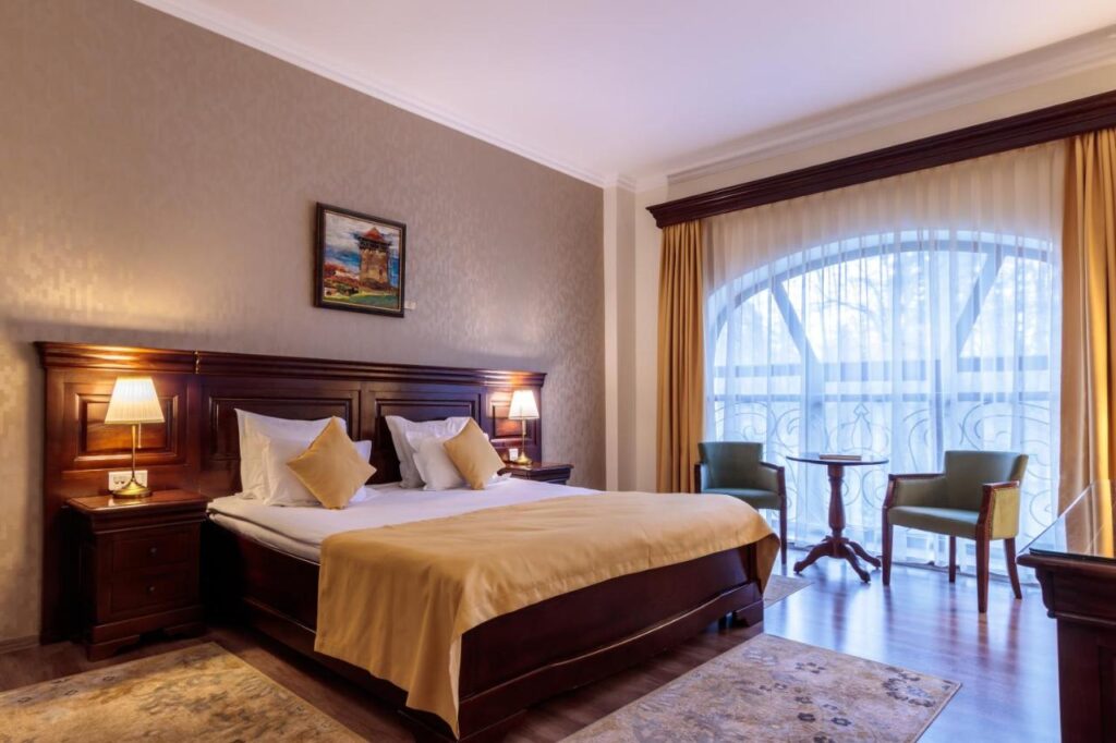 Dormitor cu pat dublu, mobilier închis și fereastră mare arcuită.