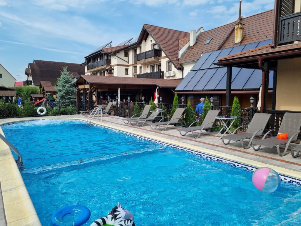 Piscină exterioară cu șezlonguri, lângă clădiri cu acoperișuri înclinate.