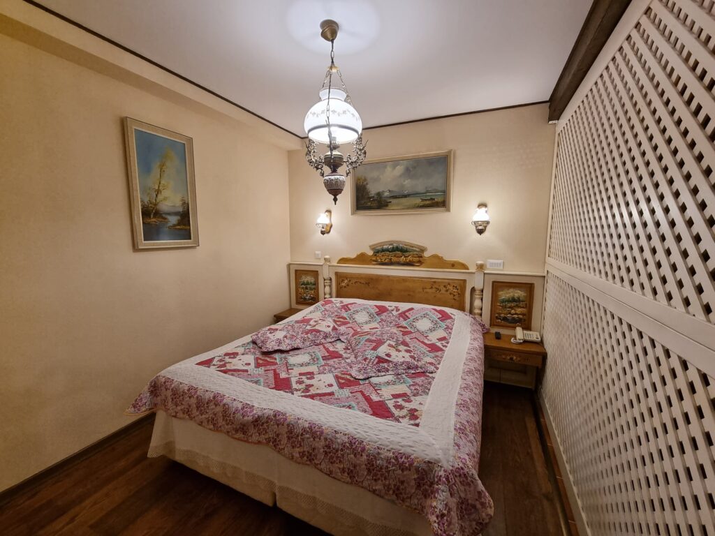 Dormitor cu pat dublu, cuvertură florală și perete decorativ alb.
