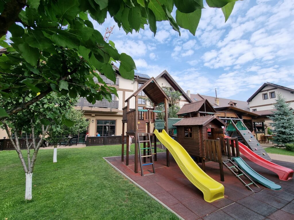 Loc de joacă din lemn, cu tobogane colorate și gazon.