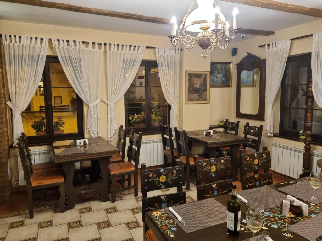 Sală de mese cu mobilier din lemn, perdele albe și candelabru.