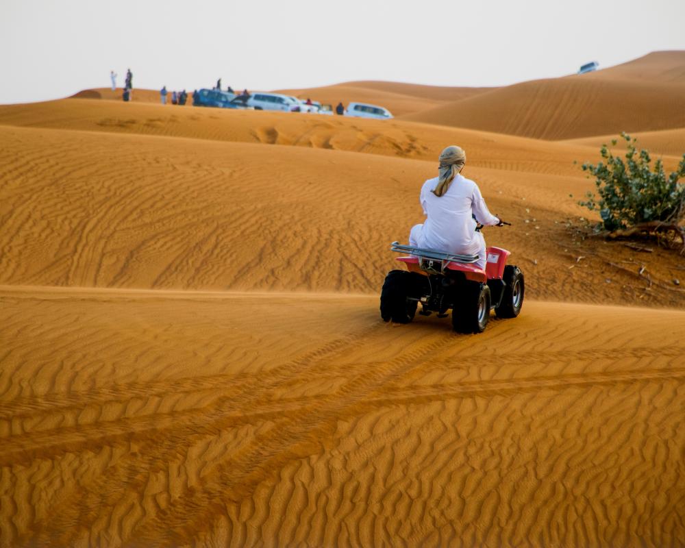 Persoană conducând un vehicul de teren pe dune de nisip.