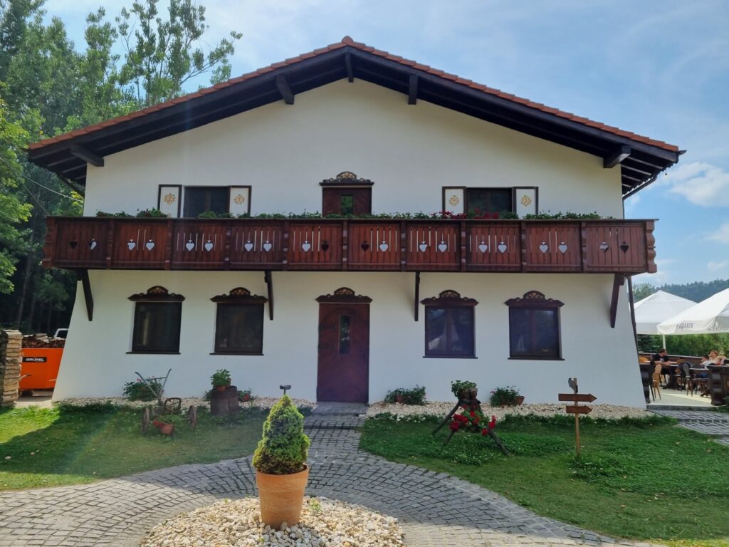 Casă albă cu balcon lung din lemn și alee pietruită.