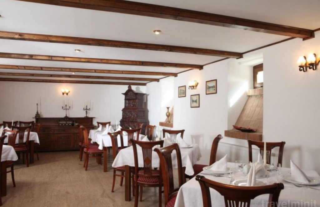 Restaurant cu mese acoperite în alb și grinzi din lemn.