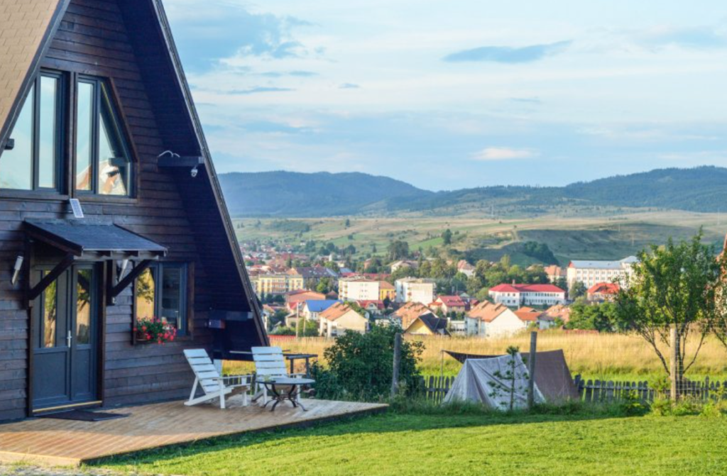 Cabană triunghiulară pe un deal, cu vedere spre o localitate.
