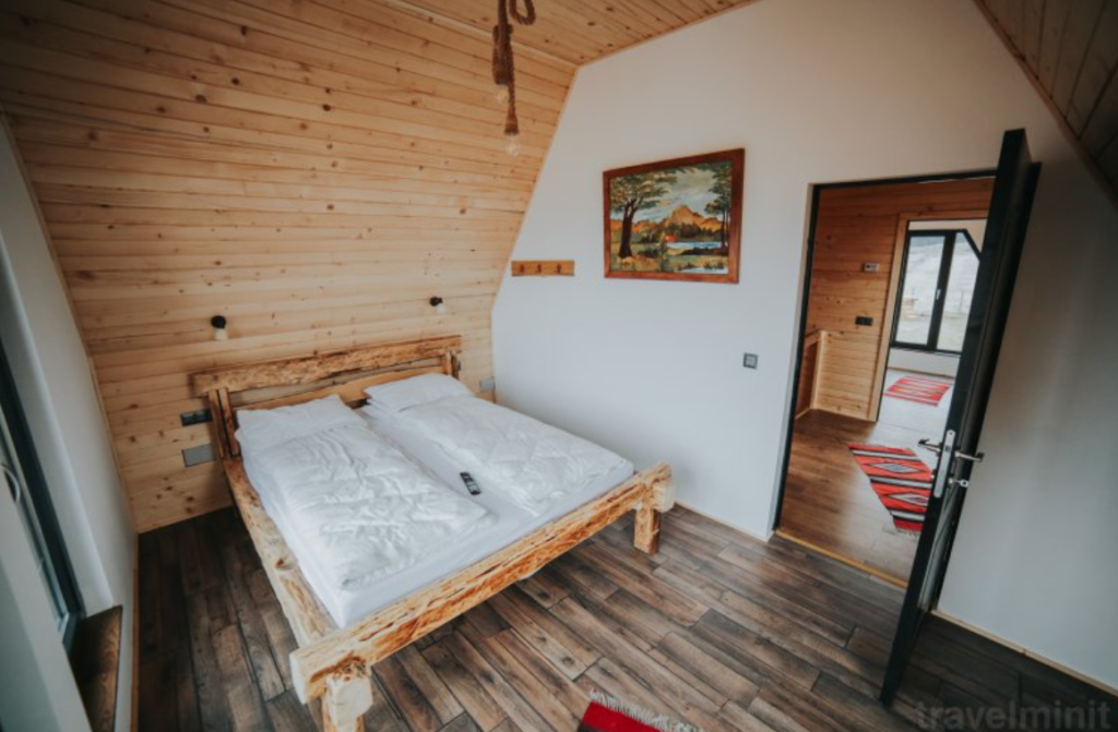 Dormitor cu pat din lemn și perete înclinat lambrisat.