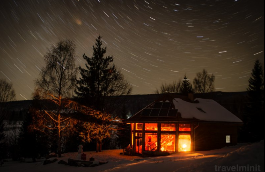 Cabană luminată noaptea, sub cer cu dâre de stele.