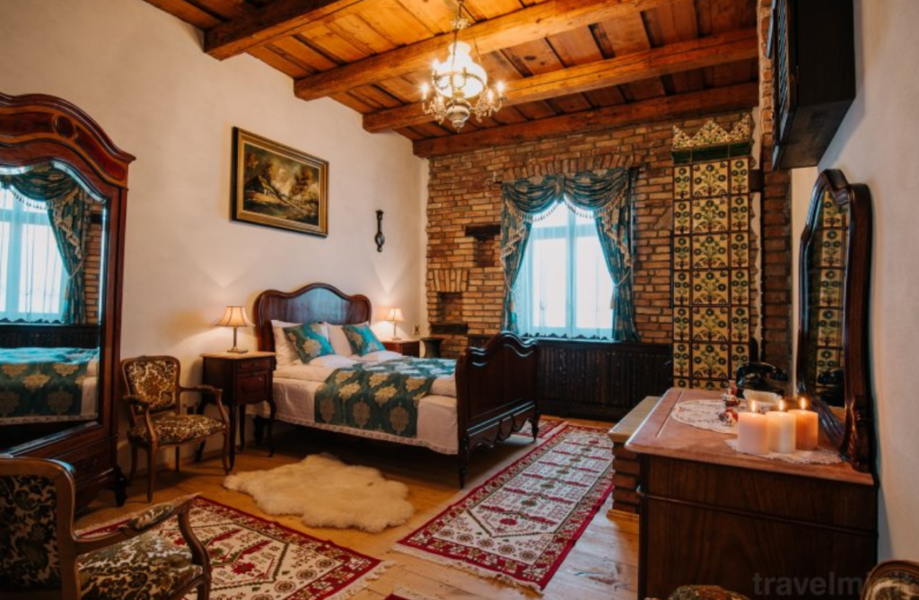 Dormitor rustic cu pat sculptat, covor și tavan din lemn.