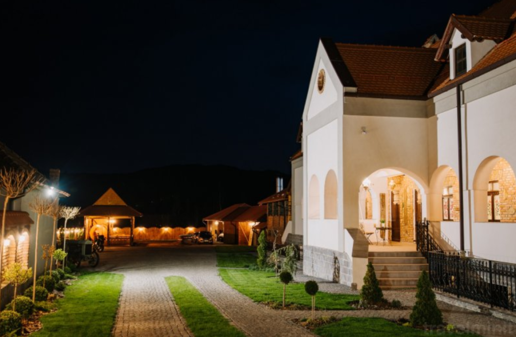 Clădire albă cu arcade iluminate, lângă o alee nocturnă.