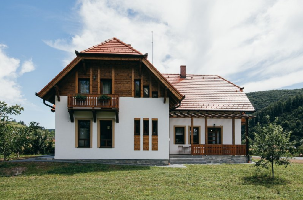 Casă albă cu balcon din lemn și acoperiș din țiglă.