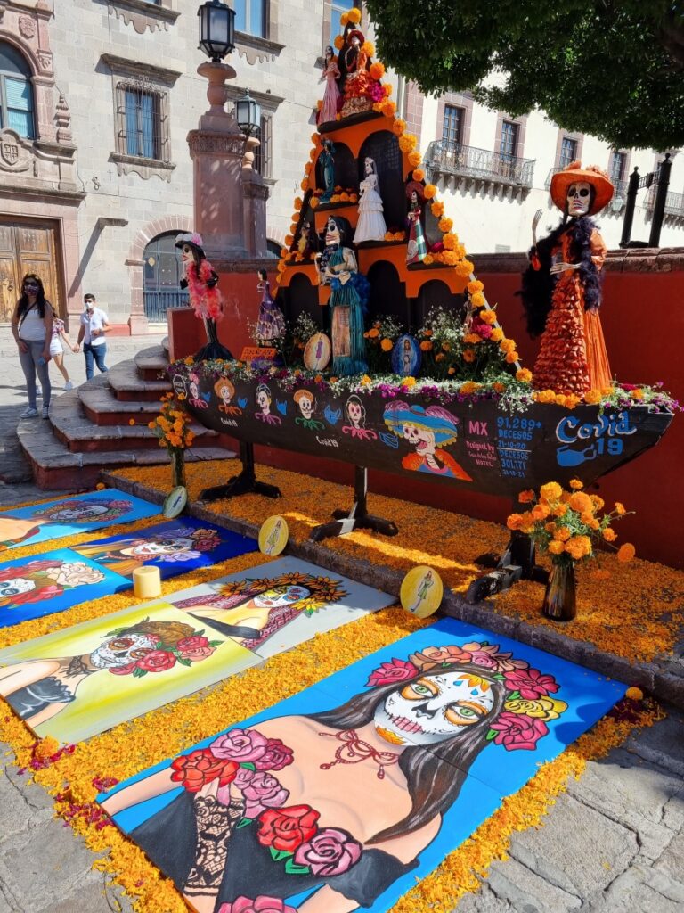 Altar festiv cu flori și decorațiuni, lângă un covor colorat pe pavaj.