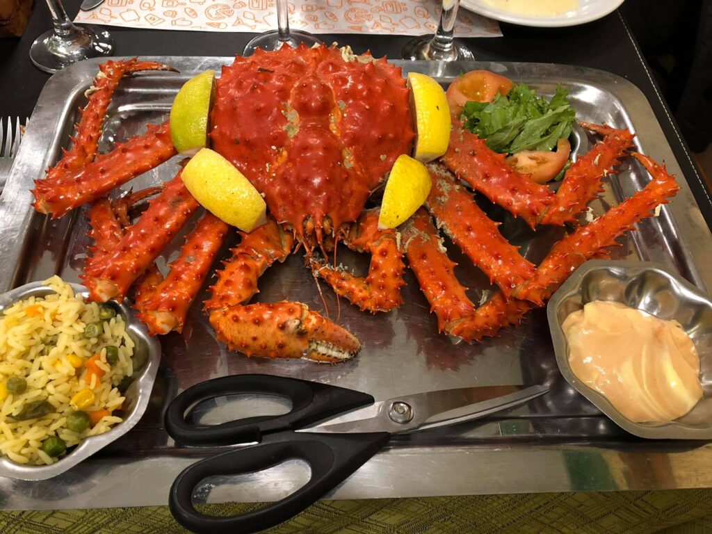 Crab roșu servit pe platou, cu lămâie și garnituri.