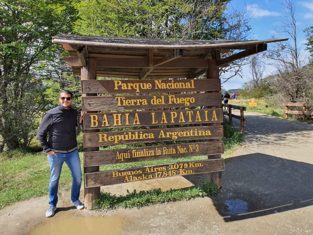 Bărbat lângă un panou din lemn, la marginea pădurii.