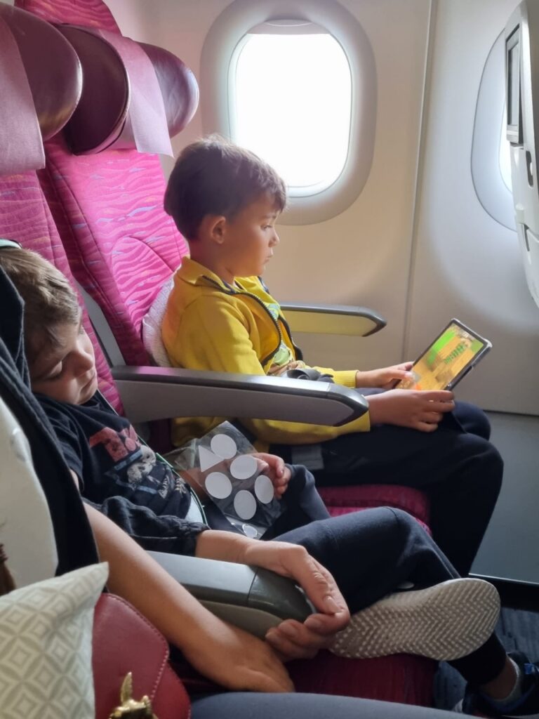 Copil privind o carte pe un scaun de avion, lângă hublou.