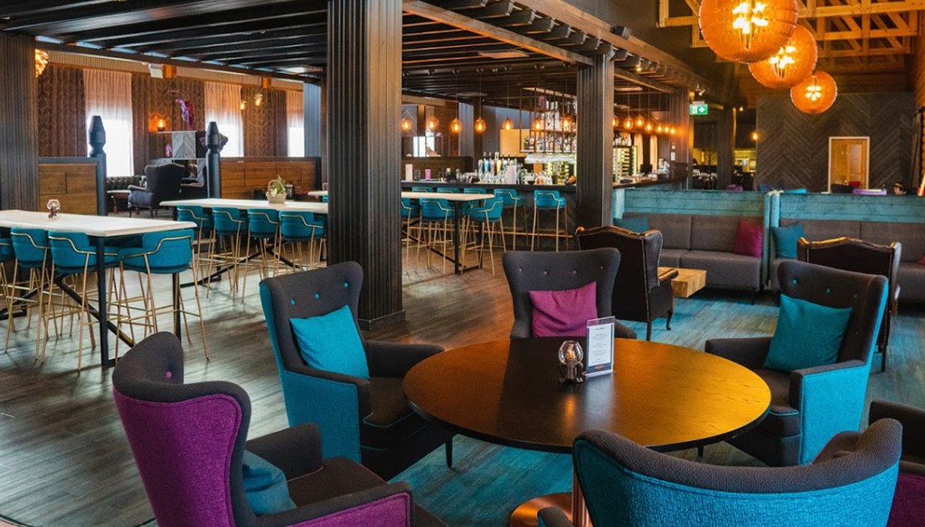 Restaurant cu fotolii colorate, mese rotunde și corpuri de iluminat sferice.