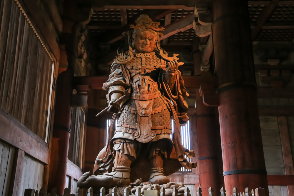 Statuie monumentală într-un interior cu stâlpi din lemn