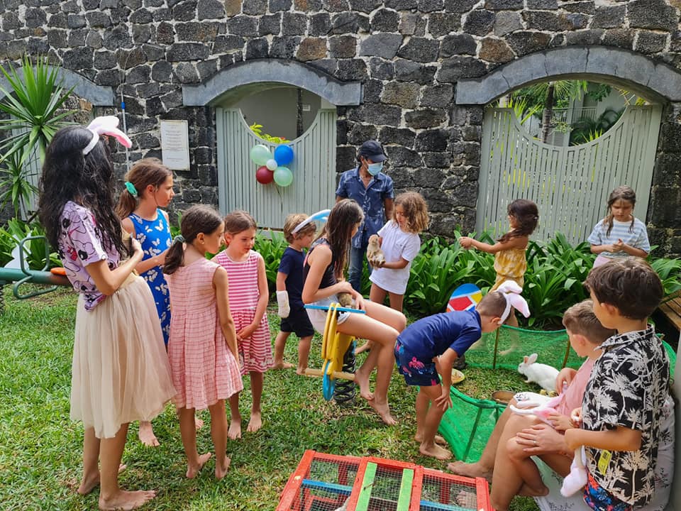 Grup de copii și adulți așezați în cerc, într-o curte.
