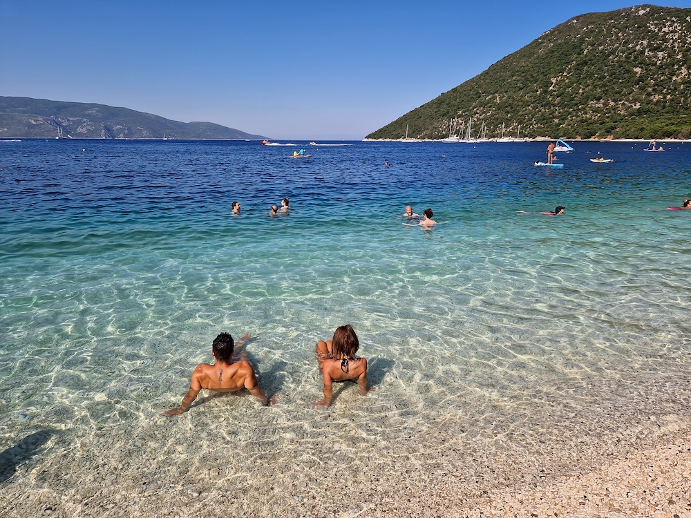 Turiști înotând în apa limpede de la Antisamos