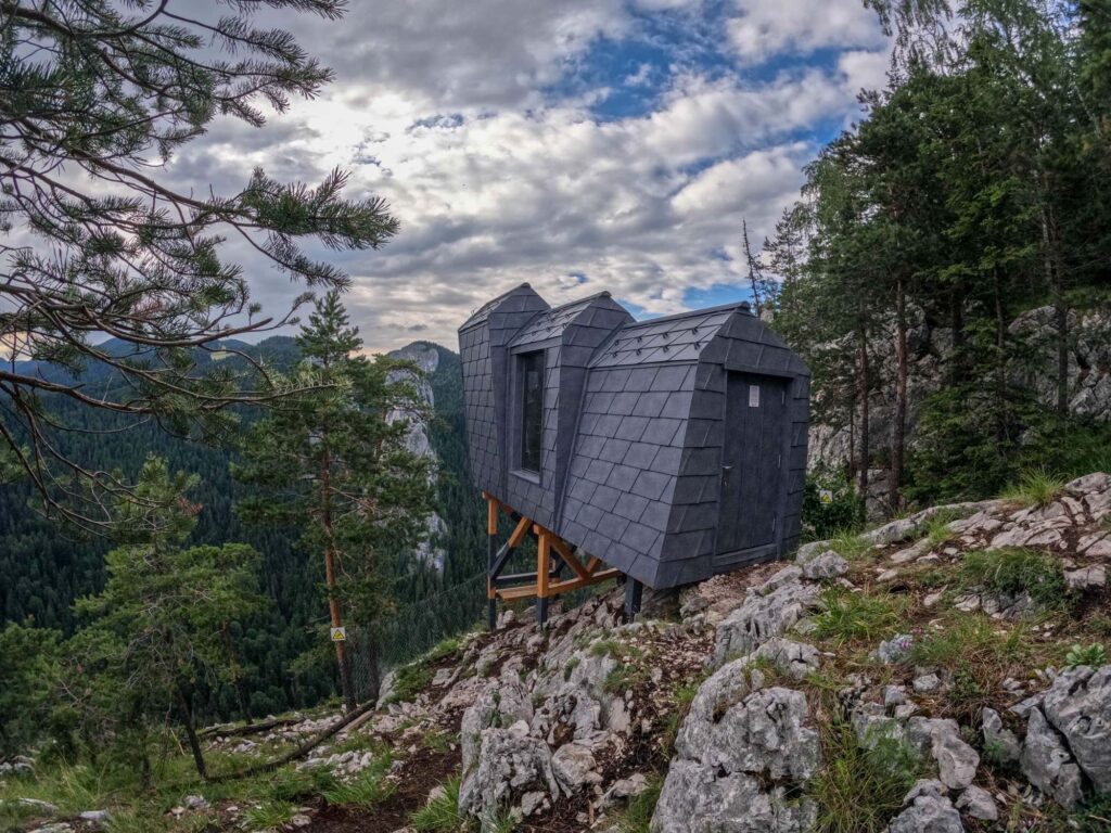 Cabane mici pe un versant stâncos, între arbori.