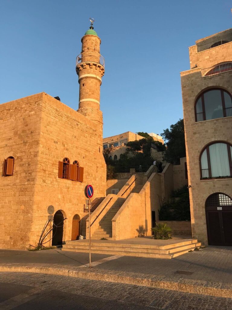 Clădire din piatră cu minaret și scară exterioară, sub cer senin.