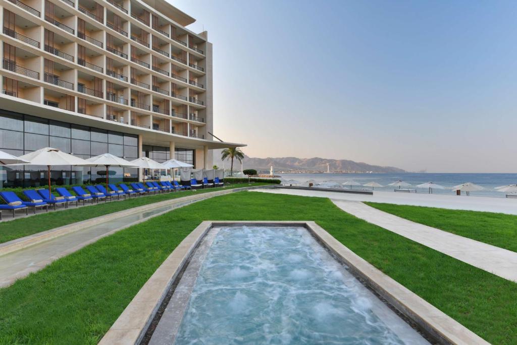 Clădire cu balcoane lângă piscine, gazon și mare.