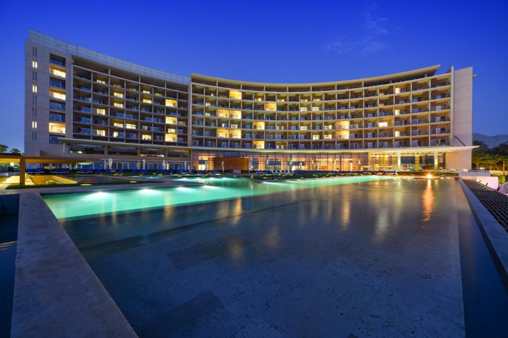 Clădire curbată și piscine iluminate la lăsarea serii.