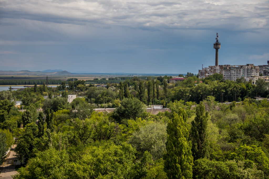 Panoramă cu arbori, blocuri și un turn înalt sub cer înnorat.