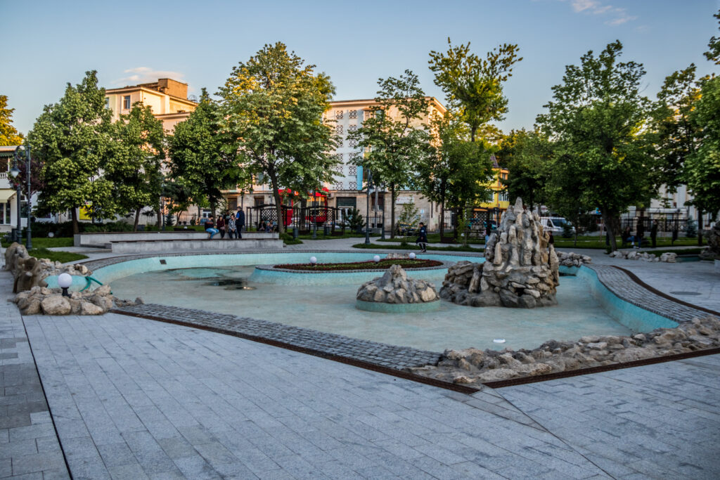 Bazin ornamental gol, cu grupuri de pietre, într-o piațetă cu arbori.