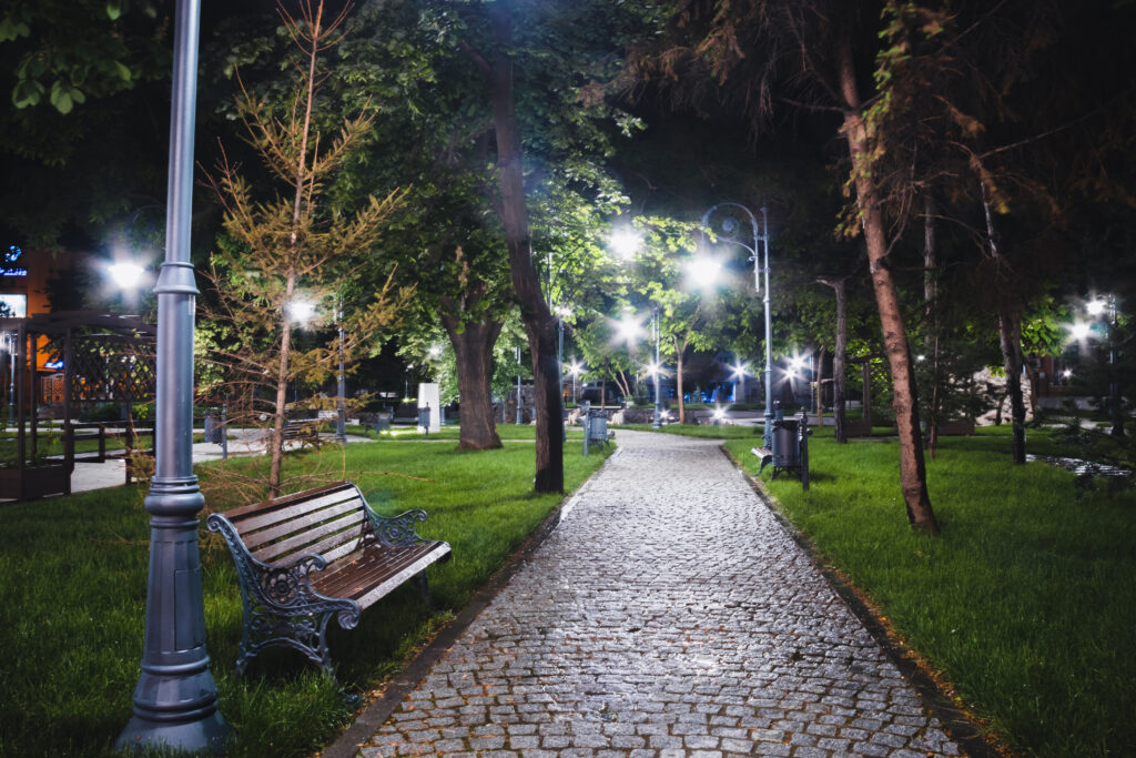Alee pavată cu bănci și felinare aprinse, într-un parc noaptea.