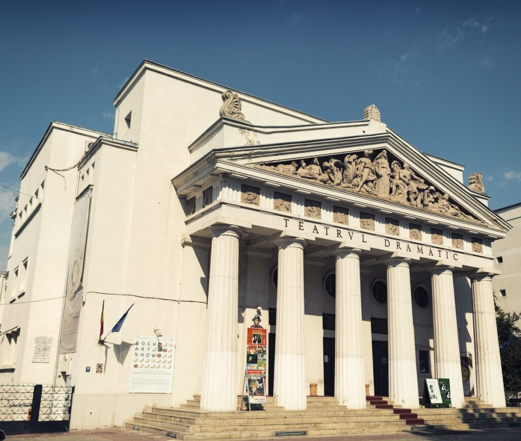 Clădire de teatru cu coloane înalte și fronton sculptat.