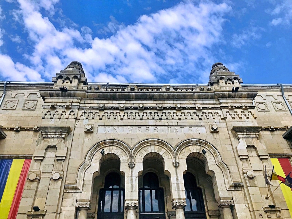 Fațadă ornamentată din piatră, cu arcade și drapele românești.