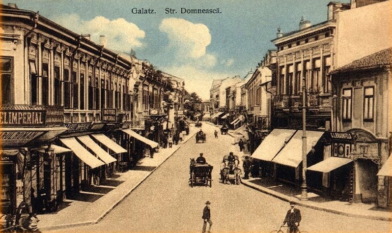 Carte poștală veche cu o stradă comercială și trăsuri.
