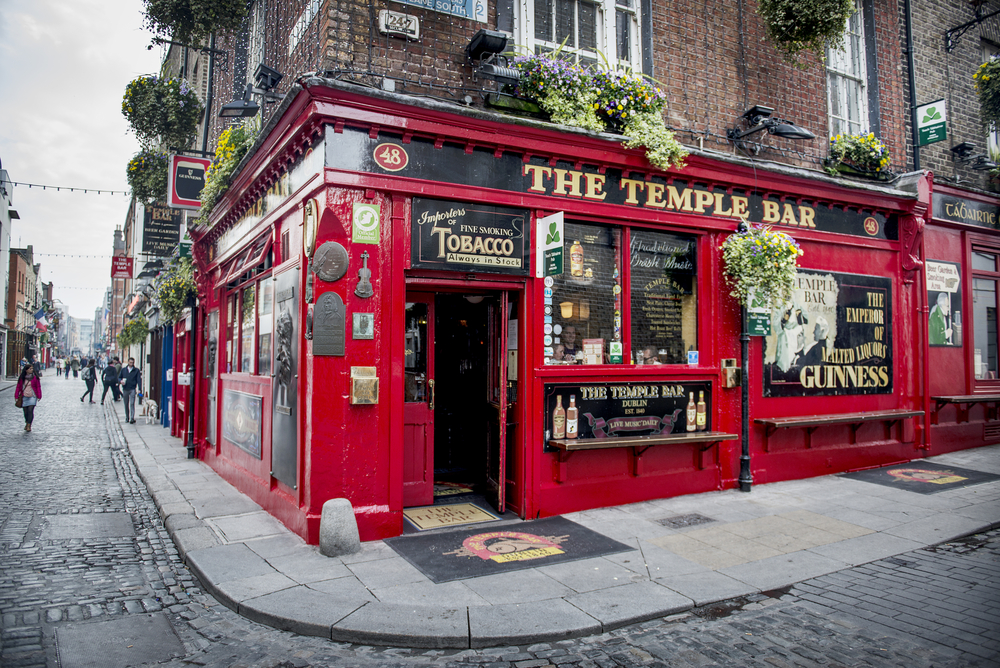 Local de colț cu fațadă roșie, flori și firma The Temple Bar.