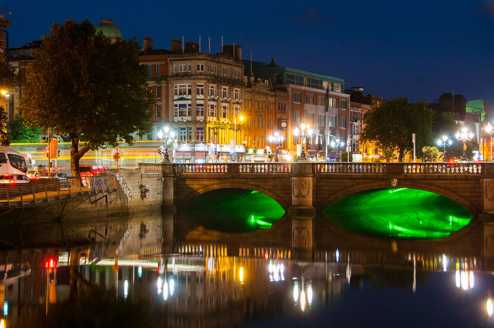 Pod de piatră iluminat cu verde, reflectat în râu noaptea.
