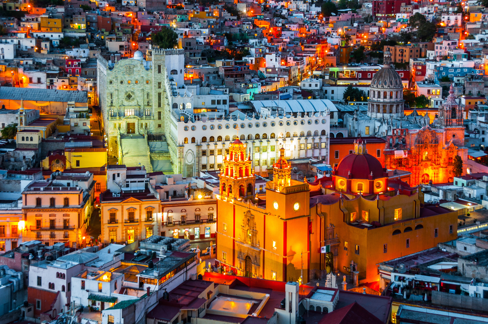 Panoramă urbană la amurg, cu o biserică galbenă între clădiri colorate.
