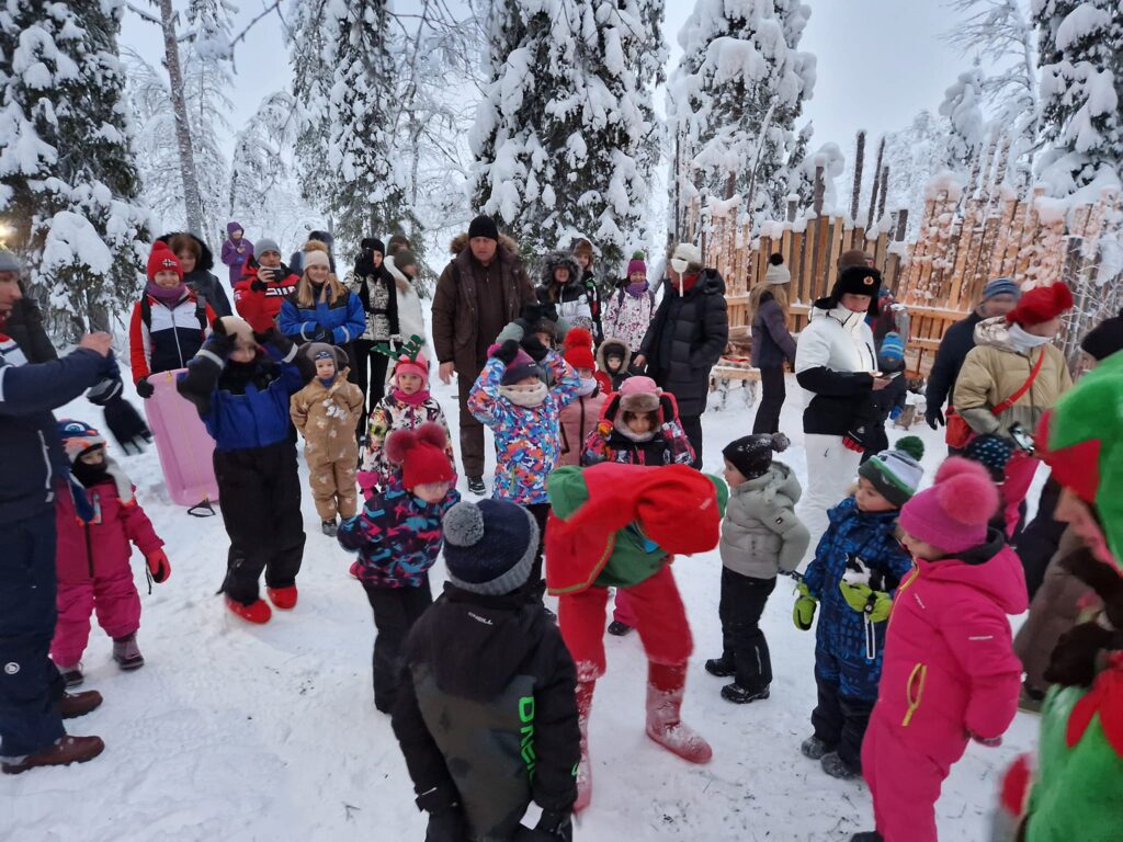 Grup de copii și adulți adunați în cerc într-o pădure înzăpezită.