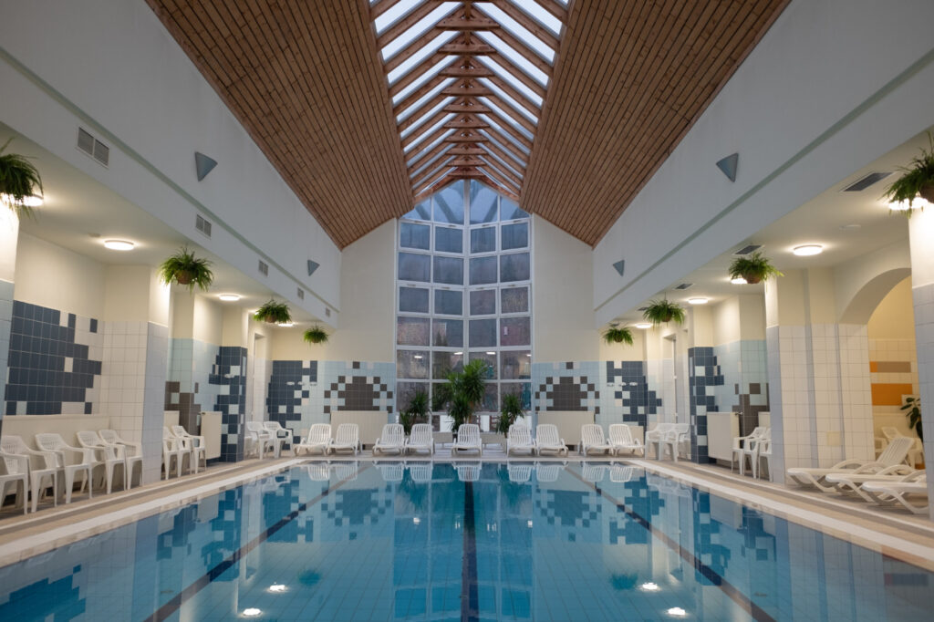 Piscină interioară cu șezlonguri, pereți cu mozaic și luminator în acoperiș.