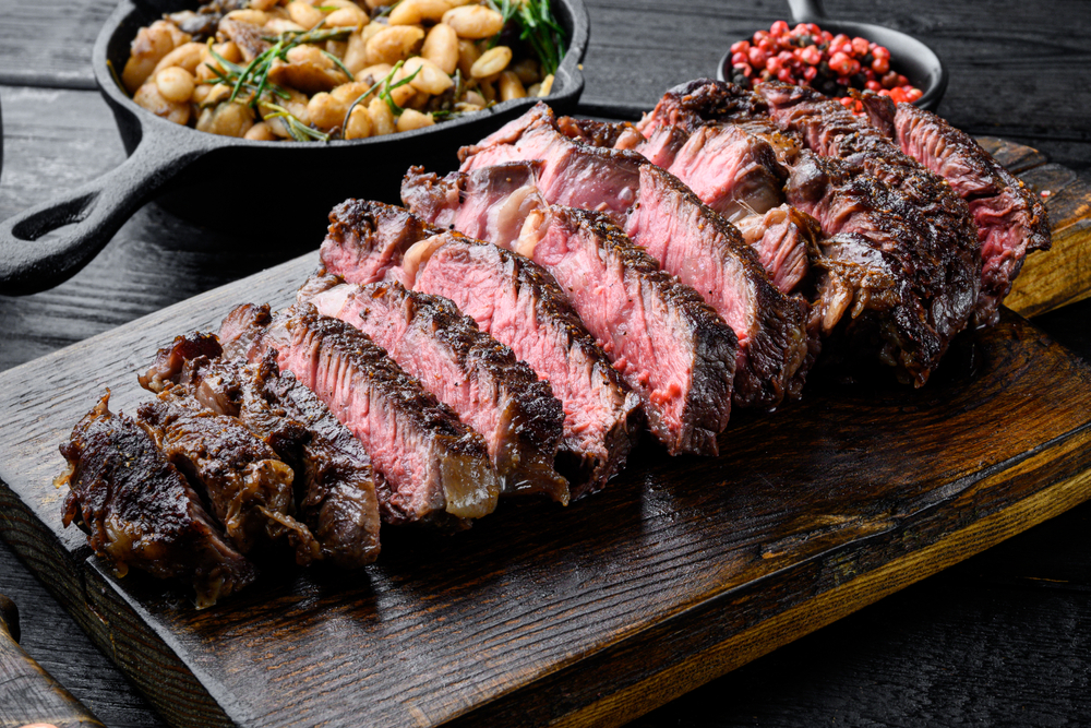 Carne friptă feliată pe un tocător, lângă garnituri.