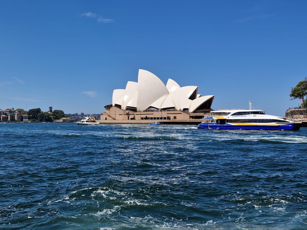 Opera din Sydney văzută peste apă, sub cer albastru