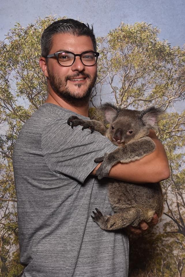 Bărbat cu ochelari ținând un koala în brațe