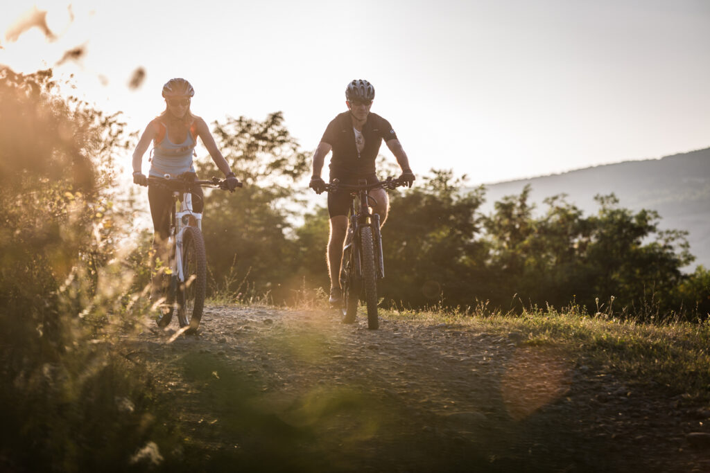 Doi bicicliști pe o potecă, în lumina joasă a soarelui.