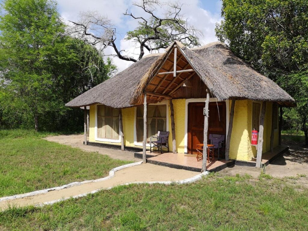 Cabană cu acoperiș de stuf și verandă, înconjurată de vegetație.