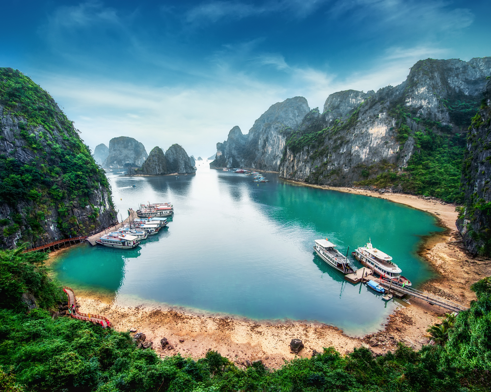 Golf liniștit cu stânci împădurite, plajă și bărci acostate.