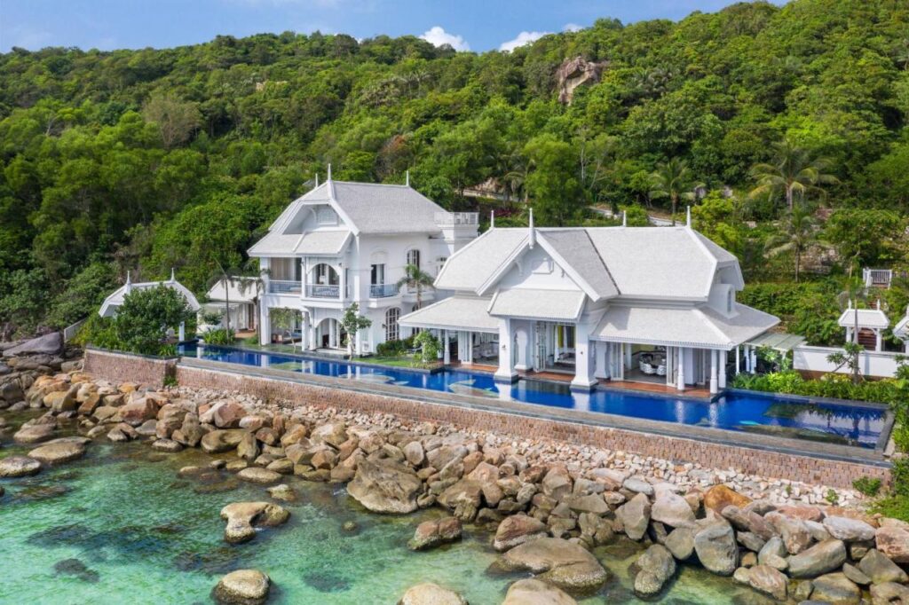 Vile albe cu piscine, pe un țărm stâncos lângă pădure.