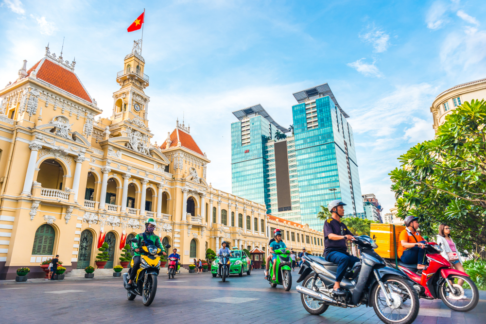 Motociclete în fața unei clădiri ornamentate, cu turn și acoperișuri roșii.