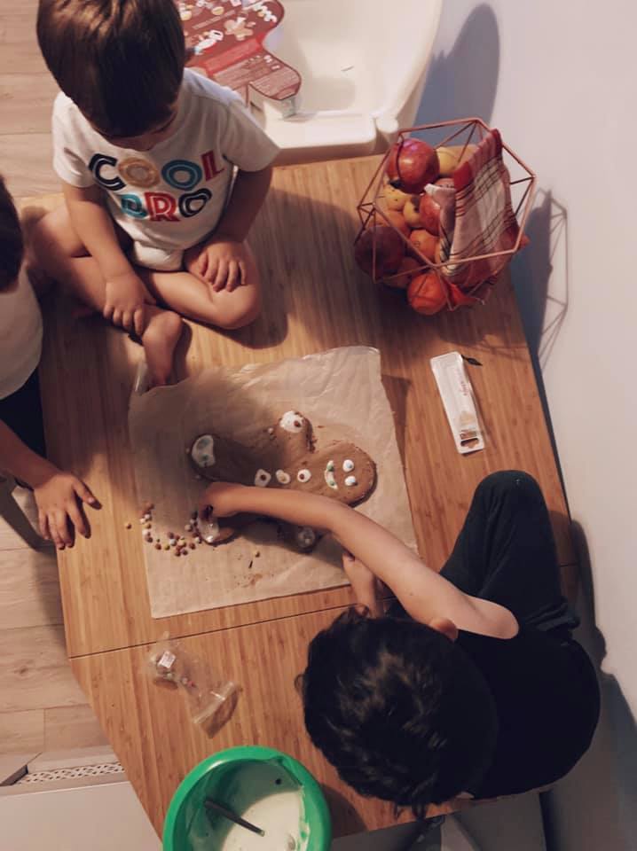Copii și un adult decorând biscuiți pe o masă din lemn.