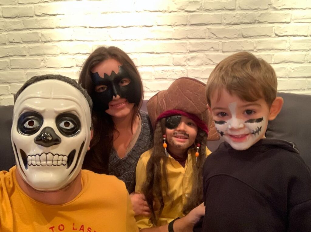 Adulți și copii purtând măști și costume, în fața unui perete de cărămidă.