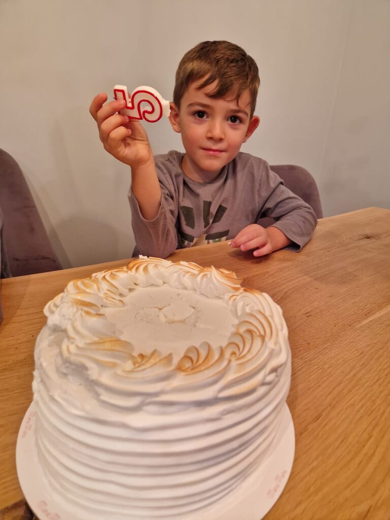 Copil la masă lângă un tort alb, ținând o decorațiune aniversară.