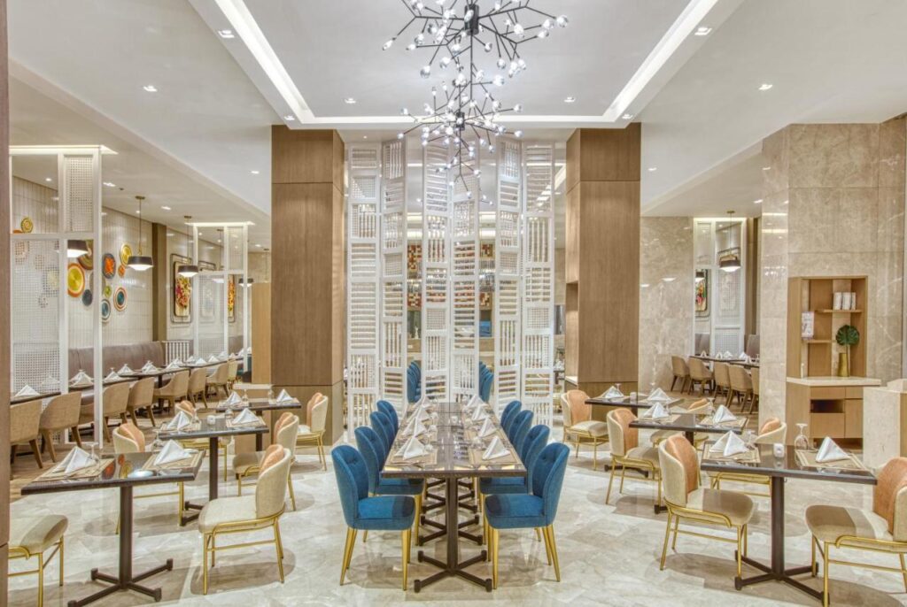 Restaurant cu mese pregătite, scaune albastre și candelabre.