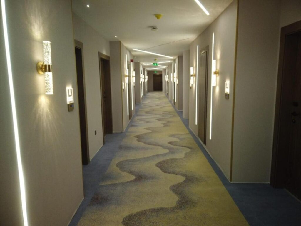 Coridor lung cu uși, aplice și mochetă cu model ondulat.